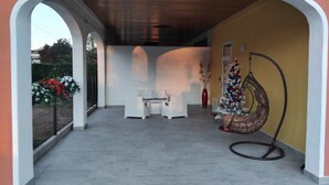 An outdoor covered patio area with white wicker furniture, a Christmas tree, and a hanging chair. - Detached house with private parking 250 meters from the spa train station (Montegrotto Terme)
