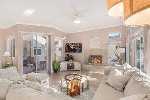 Ein geräumiges Wohnzimmer mit Kamin, einem an der Wand befestigten Fernseher und einer Schiebeglastür, die zu einem Außenbereich führt.