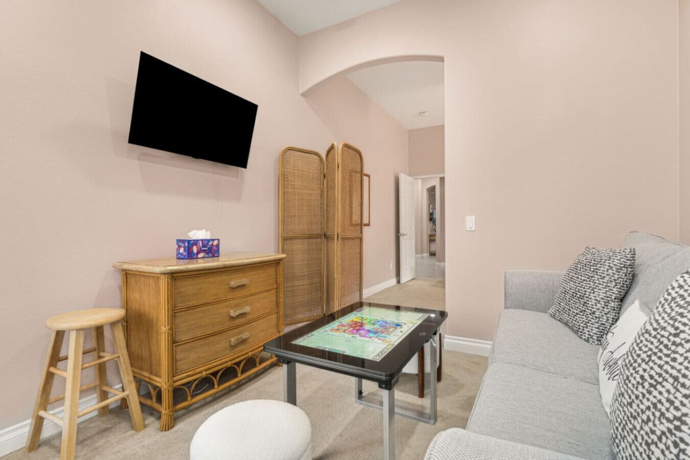 A room with a television mounted on the wall, a wooden dresser, a glass coffee table, and a grey sofa.