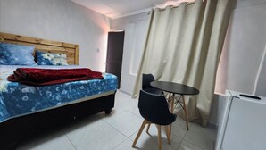 Een slaapkamer met een bed, een rode deken, een blauwe bloemenbedspreider, een klein zwart tafeltje en een stoel.