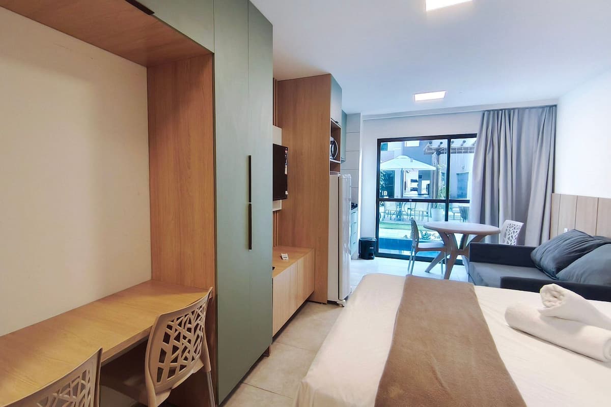Habitación de hotel con cama, escritorio, silla, televisión y balcón con vistas.