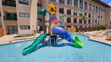 Piscina com escorregadores e área de recreação aquática, cercada por um edifício com vários andares e varandas.