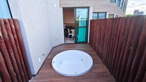 Un jacuzzi en un espacio exterior reducido, con una valla de madera en un lado y la entrada de un edificio en el otro.