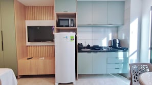 Un espacio habitable compacto con televisor, refrigerador, microondas y kitchenette.