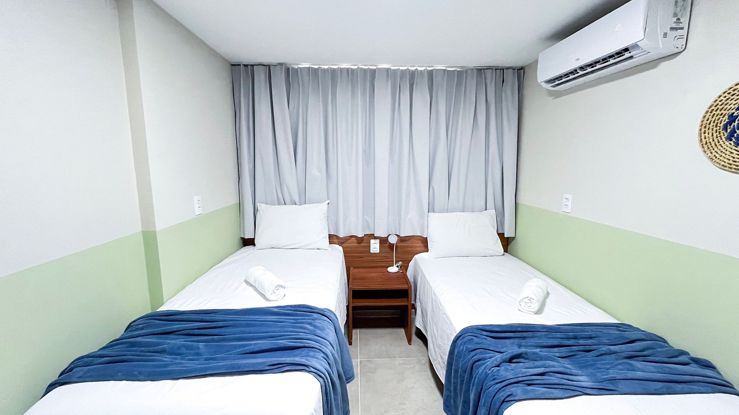 A hotel room with two single beds, a wooden nightstand, a small table, and an air conditioning unit.