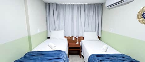 A hotel room with two single beds, a wooden nightstand, a small table, and an air conditioning unit.