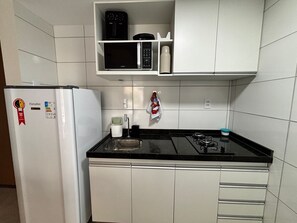 Una cucina compatta con un frigorifero bianco, un forno a microonde, un piano cottura a gas e un lavello.