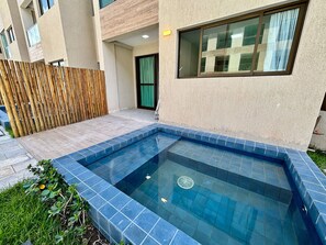 A swimming pool with blue tiles, a wooden fence, and a building with a window. - Max Carneiros Suites - Com e sem Piscina Privativa (Tamandaré)