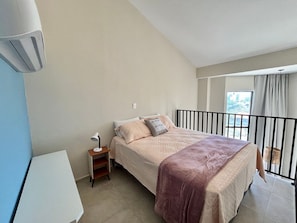 Une chambre à coucher avec un lit, une table de chevet, une lampe et une vue sur l’extérieur.