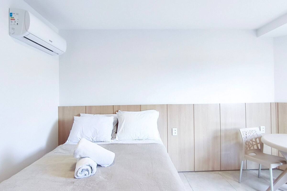 Una habitación de hotel con una cama, una mesa y un equipo de aire acondicionado.