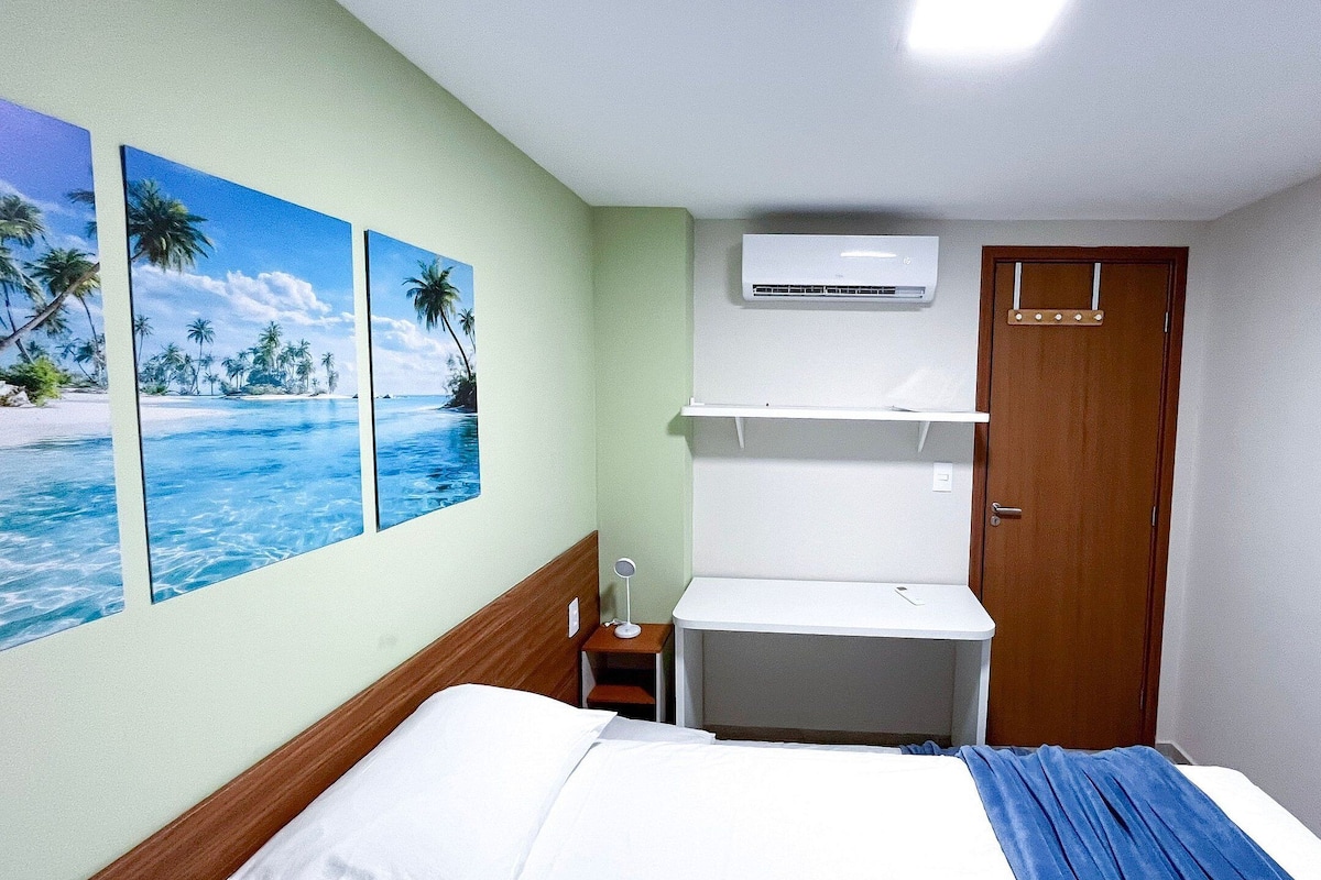 Una habitación de hotel con cama, mesita de noche, aire acondicionado de pared y una puerta.