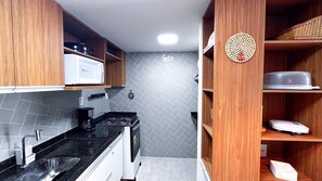A compact kitchen with a gas stove, a microwave, and wooden cabinets. - Max Carneiros Suites - Com e sem Piscina Privativa (Tamandaré)