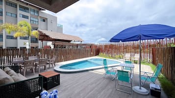 Uma área de piscina com deck de madeira, espreguiçadeiras e um espaço de estar coberto.