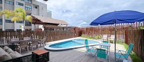 Et poolområde med træterrasse, liggestole og en overdækket siddeplads.