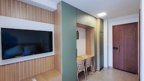 Une pièce avec un téléviseur fixé au mur, un bureau avec une chaise et une porte en bois.