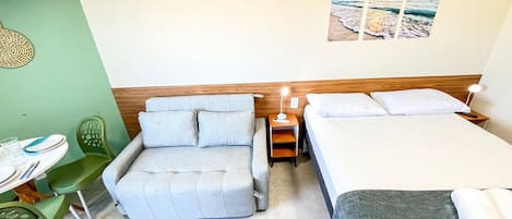 A hotel room with a bed, a sofa, a small table with a chair, and a wall-mounted picture.