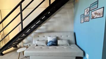 Uma sala de estar moderna com um sofá, uma mesa redonda pequena, uma escada e quadros nas paredes.