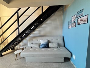 A modern living room with a sofa, a small round table, a staircase, and framed pictures on the wall. - Max Carneiros Suites - Com e sem Piscina Privativa (Tamandaré)