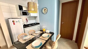 A compact kitchen with a refrigerator, microwave, and stove, a dining table set with plates and glasses, and a blue accent wall. - Max Carneiros Suites - Com e sem Piscina Privativa (Tamandaré)