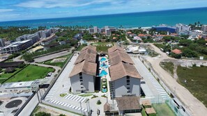 An aerial view of a hotel with a swimming pool, surrounded by greenery and a view of the ocean. - Max Carneiros Suites - Com e sem Piscina Privativa (Tamandaré)