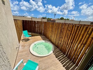 Un cortile con una vasca idromassaggio, due poltrone verdi e un recinto in legno.