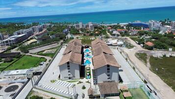 Vista aérea de um hotel com piscina, rodeado por vegetação e vista para o oceano.