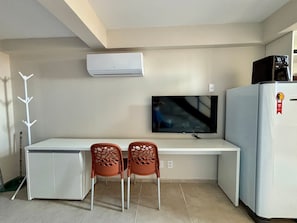 Una kitchenette compacta con un televisor, un refrigerador y dos sillas.