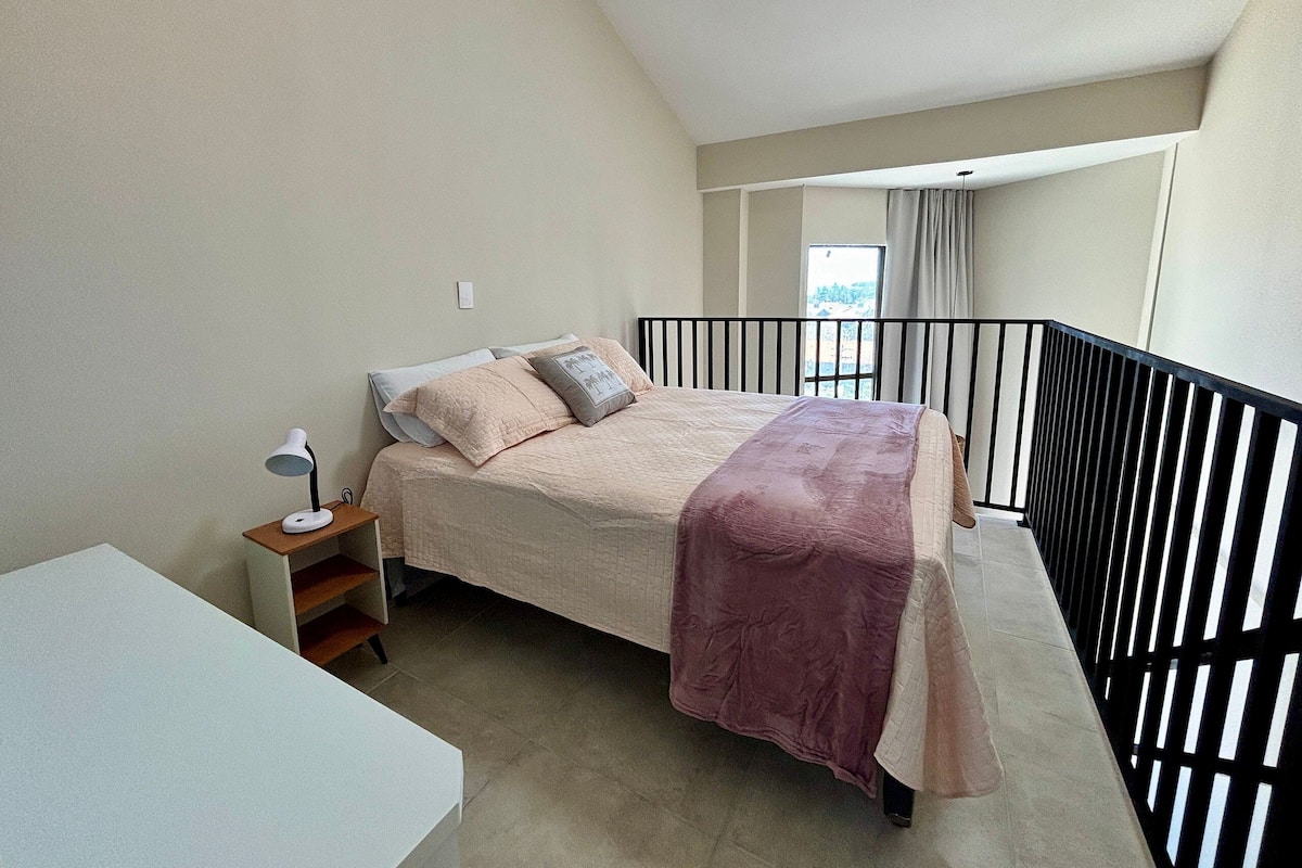 Un dormitorio con cama, mesita de noche, lámpara y vistas al exterior.