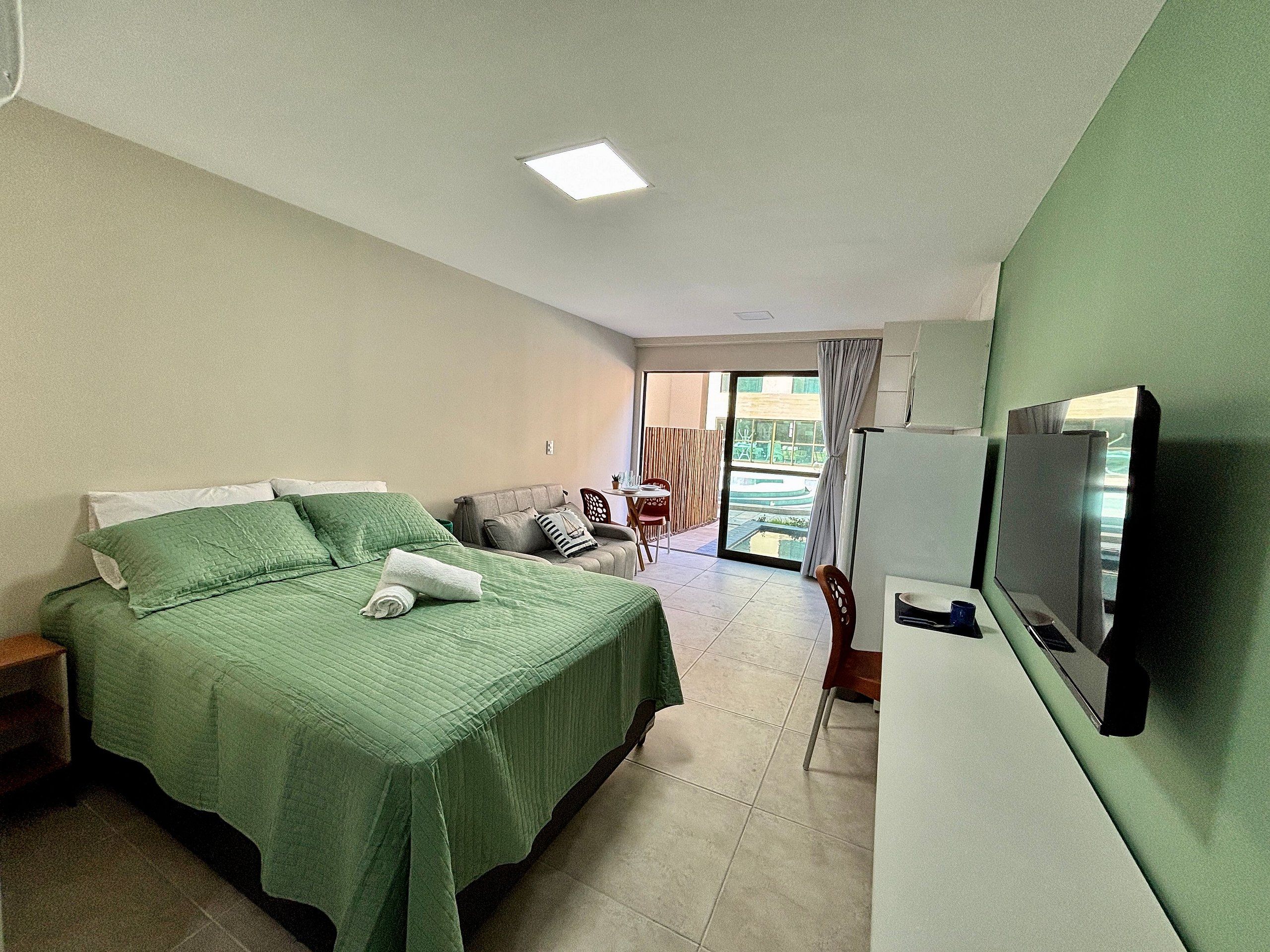 Quarto de hotel com cama, televisão, área de refeições e vista para o exterior.