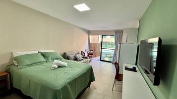 Quarto de hotel com cama, televisão, área de refeições e vista para o exterior.