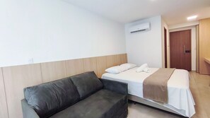 A hotel room with a bed, a sofa, an air conditioning unit, and a door. - Max Carneiros Suites - Com e sem Piscina Privativa (Tamandaré)
