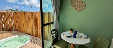 A room with a view of the sky, a wooden fence, a hot tub, a table with plates, and two chairs.