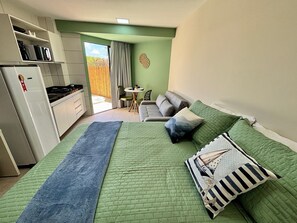 Egy hálószoba, amelyben található egy ágy, egy kanapé, egy étkezőasztal és egy konyhasarok, ahol egy hűtőszekrény is van.