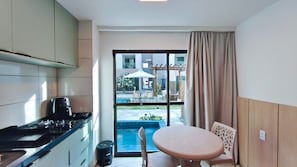 Une cuisine moderne dotée d’une cuisinière intégrée, un coin repas avec une table et des chaises, et une grande fenêtre donnant sur une piscine et un espace de détente extérieur.