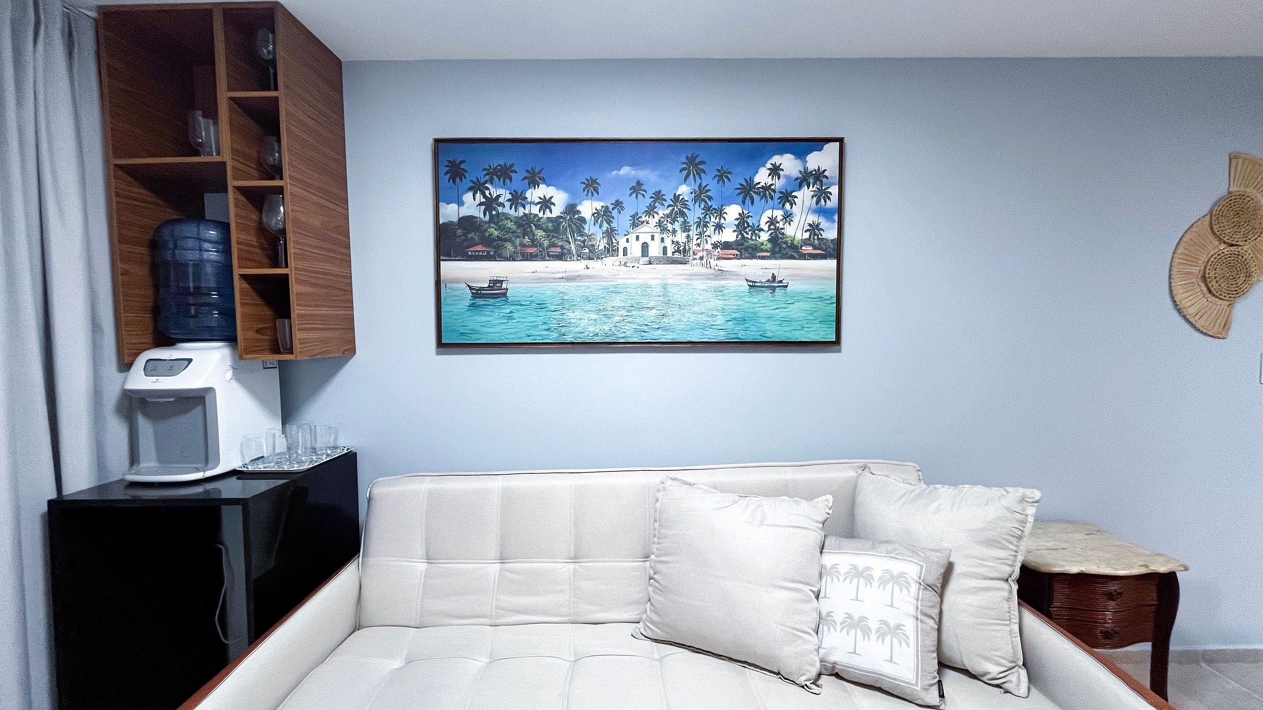 A living room with a white sofa, a coffee machine, a water dispenser, and a framed tropical beach painting.