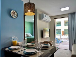 A dining area with a table set for four, a large mirror, and an air conditioning unit on the wall. - Max Carneiros Suites - Com e sem Piscina Privativa (Tamandaré)