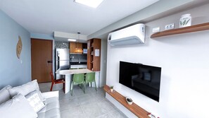 A compact living space with a kitchenette, a dining area, a sofa, and a mounted TV. - Max Carneiros Suites - Com e sem Piscina Privativa (Tamandaré)