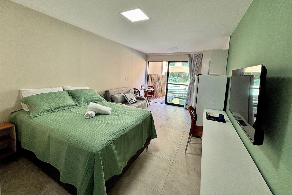Habitación de hotel con cama, televisión, zona de comedor y vistas al exterior.