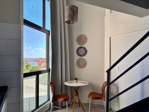 Una habitación con un ventanal grande, una mesa redonda con sillas y tres adornos en la pared.
