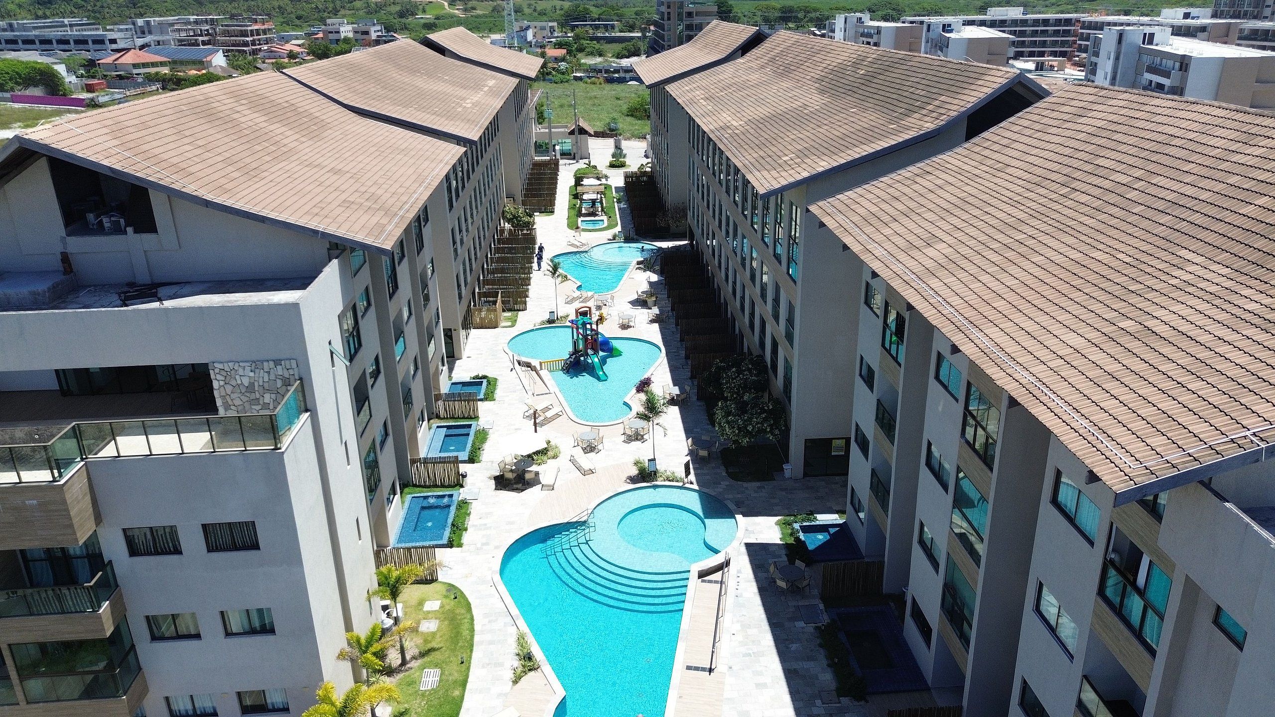 Un hotel de varios pisos con una piscina central, varias piscinas más pequeñas y zonas de estar al aire libre.