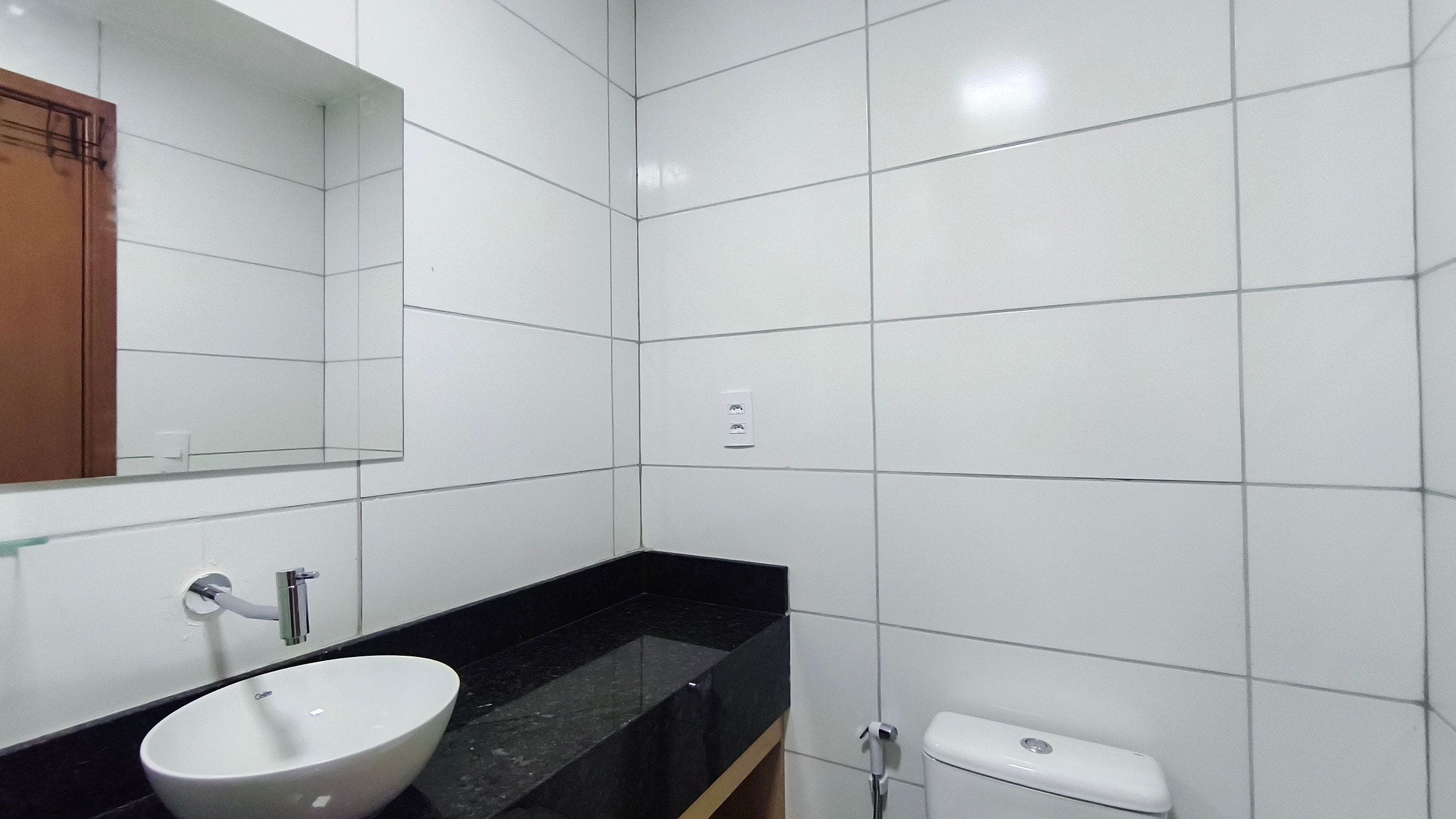 Een badkamer met witte tegels, een witte wasbak, een zwart aanrecht en een toilet.
