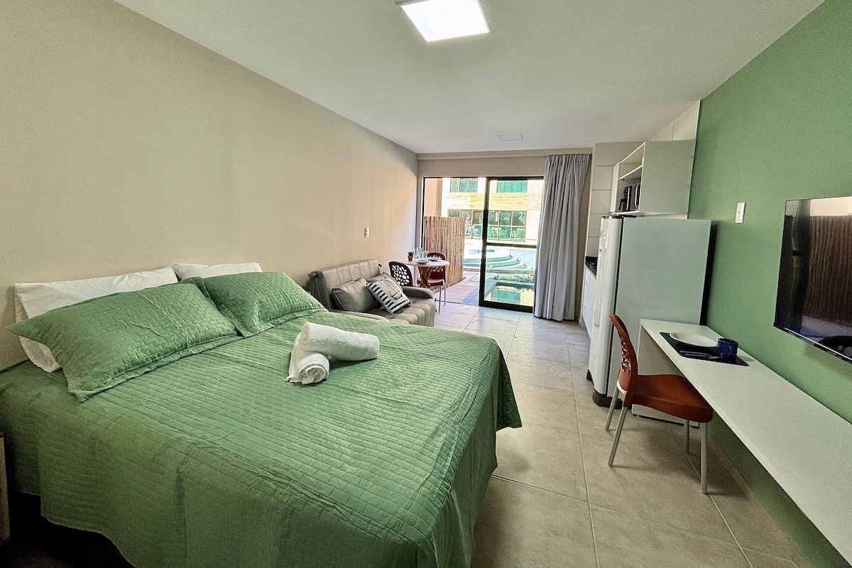 Habitación de hotel con cama, escritorio, silla, televisión y puerta corrediza a un espacio exterior.