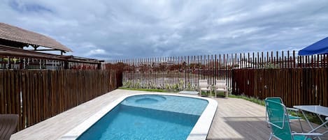 Une piscine rectangulaire entourée d’une terrasse en bois, avec une clôture en bois et quelques chaises.