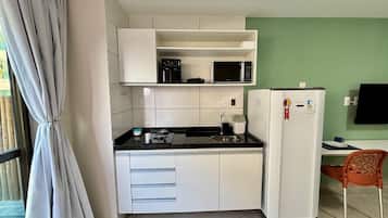 Cozinha compacta com armários brancos, micro-ondas, fogão a gás e geladeira.