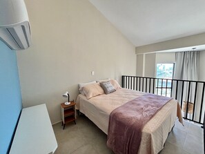 Un dormitorio con cama, mesita de noche, lámpara y vistas al exterior.