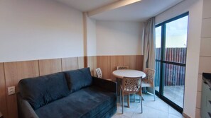Una sala moderna con un sofá azul oscuro, una mesa redonda con sillas, y un amplio ventanal corredero que da a un espacio exterior.