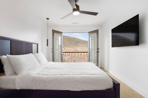 A bedroom with a bed, a ceiling fan, a TV mounted on the wall, and a balcony with a view of a rocky landscape. - Relaxing Casita with immaculate views in fantastic Hurricane location (Hurricane)
