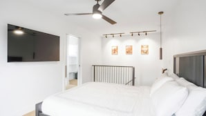 Een moderne slaapkamer met een bed, een plafondventilator, een bevestigde televisie en kunst aan de wand.