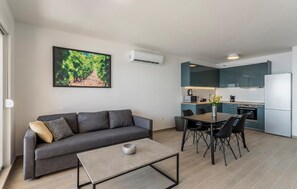 A modern living room with a grey sofa, a coffee table, and a dining area with a table and chairs. There is a kitchen with teal cabinets and a white refrigerator. - Beautiful apartment in Dingac with WiFi (Dingac)