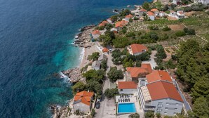 An aerial view of a coastal residential area with houses, a swimming pool, and a rocky shoreline. - Gorgeous apartment in Dingac with swimming pool (Dingac)